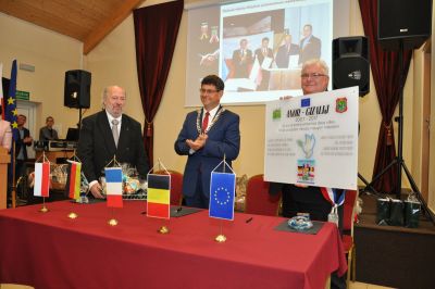 Trzech mężczyzn stoi przy stole prezydialnym, na stole flagi Polski, Niemiec, Francji, Belgii i Unii Europejskiej,...
