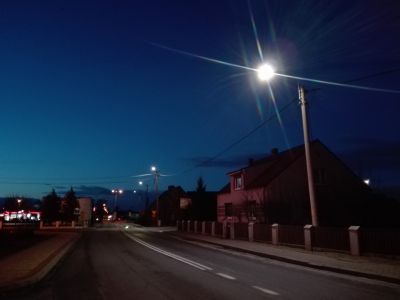 Widok ulicy z budynkami o zmroku, po lewej stronie ulicy ciąg świecących lamp